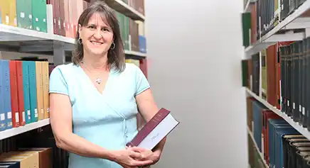 Smiling professor holding books in a library